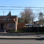 场地东侧路对面的小型私人公司、空地和公交站，在这个阳光明媚的周末中午，只有一个人在等公车。
